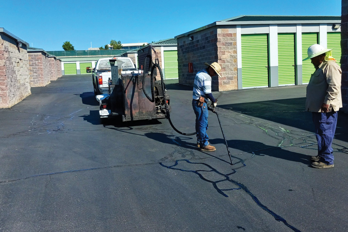 Two men applying tar to seal cracks in asphalt pavement
