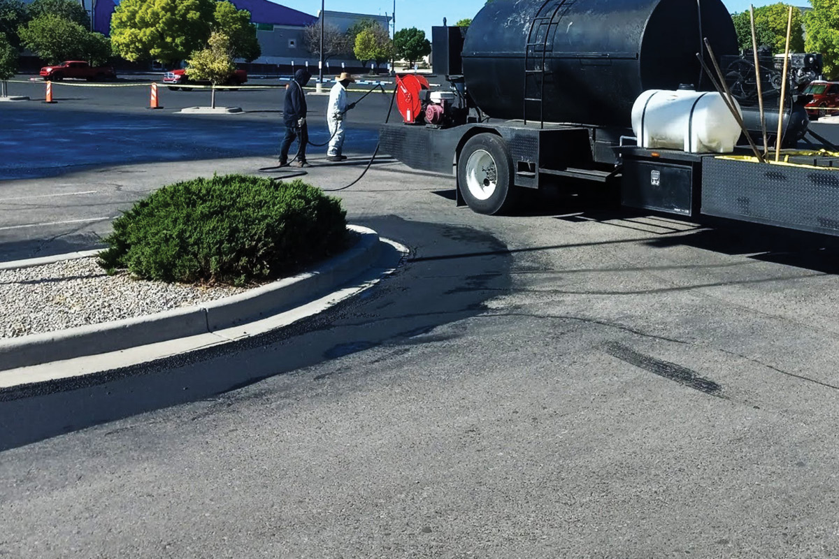 A retail parking lot with damaged asphalt being patched and sealed by a paving crew