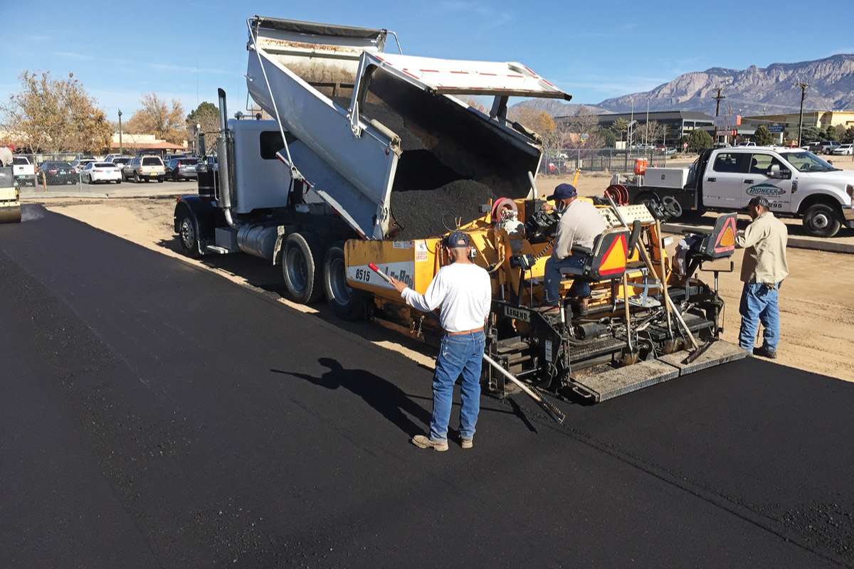A paving crew laying down a fresh asphalt parking lot, with the Sandia mountains in the background